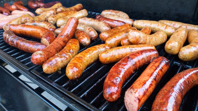 Fresh sausage and hot dogs grilling outdoors on a gas barbeque grill.