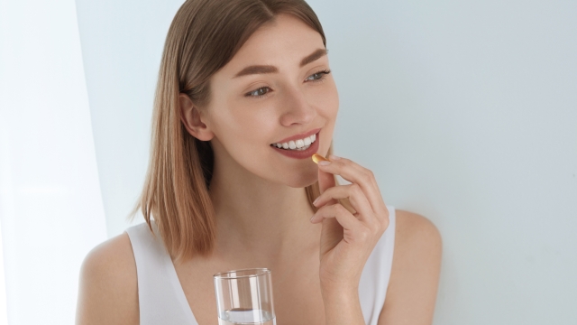 Woman taking vitamin pill with glass of fresh water indoors. Smiling girl taking omega 3 fish oil capsule, vitamin supplement. Diet nutrition concept