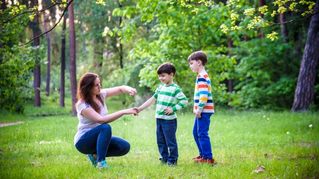 Young woman mother applying insect repellent to her two son before forest hike beautiful summer day or evening. Protecting children from biting insects at summer. Active leisure with kids.