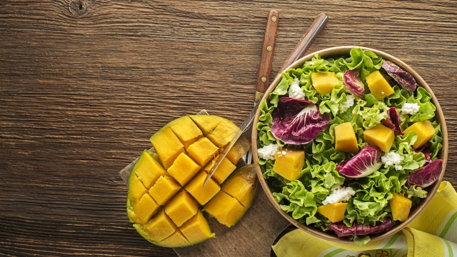 Healthy lettuce salad with mango fruit and fresh cheese on wooden table background. Healthy salad meal.