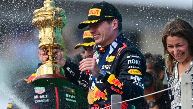 Winner Red Bull Racing's Dutch driver Max Verstappen holding the trophy reacts as second placed McLaren's British driver Lando Norris sprays champagne during the podium ceremony for the Formula One British Grand Prix at the Silverstone motor racing circuit in Silverstone, central England on July 9, 2023. (Photo by Ben Stansall / AFP)