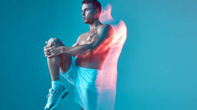 Sports workout. Athletic guy with naked torso stretching muscles, raised leg up to abs. Long exposure, motion blur. High quality photo