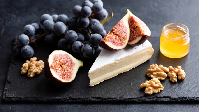 Brie or camembert cheese board with walnuts, grapes, figs and honey served on black slate plate. Gourmet appetizer