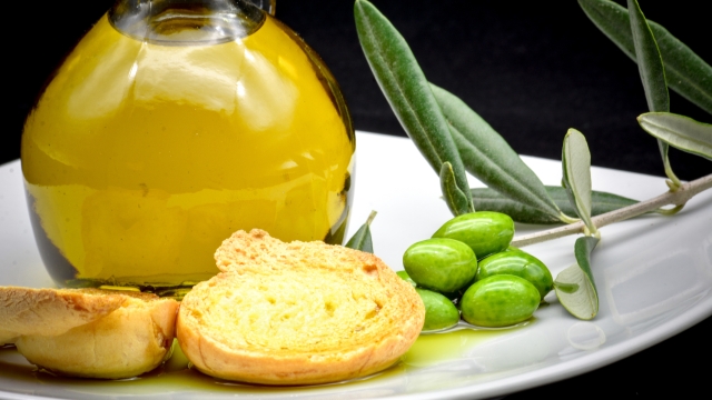 some olives and a jar full of oil and a branch of olive tree on a white dish on a black background