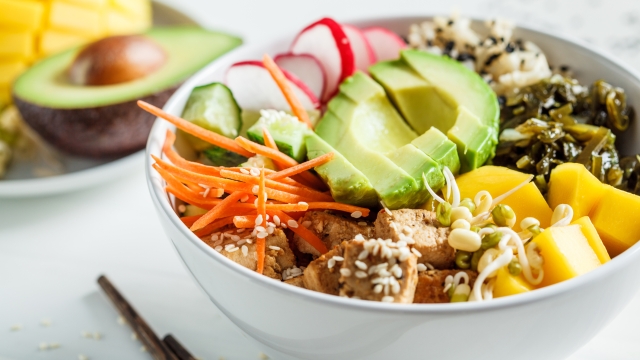 Vegan poke bowl with avocado, tofu, rice, seaweed, carrots and mangoes, white background. Vegan food concept.