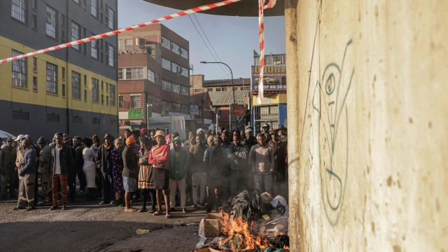 EDITORS NOTE: Graphic content / TOPSHOT - People standing at a bonfire look on as unseen firefighters work at the scene of a fire in a building in Johannesburg on August 31, 2023. At least 20 people have died and more than 40 were injured in a fire that engulfed a five-storey building in central Johannesburg on August 31, 2023, the South African city's emergency services said. (Photo by Michele Spatari / AFP)
