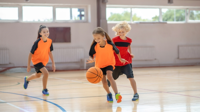 Game. Kids in bright sportswear playing basketball and running after the ball