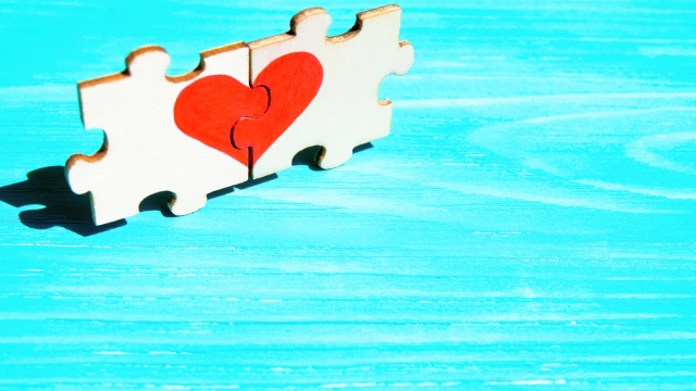 Heart symbol made from two matching jigsaw puzzle pieces on a blue wooden background. Creative romantic concept.