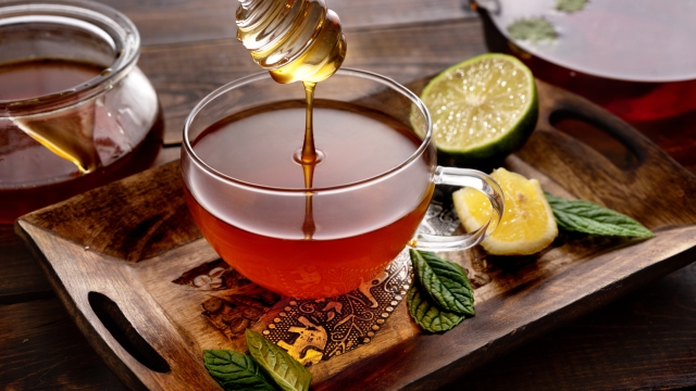 Pouring a honey glass tea cup with mint leaves and lemon on dark wooden table