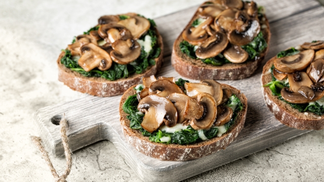 Wood board with garlic mushroom sandwiches with spinach and cheese, open faced sandwich or bruschetta with sourdough rye  bread and champignon. Light grey background.