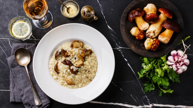 Risotto with porcini mushroom on plate and raw mushrooms on dark marble table background