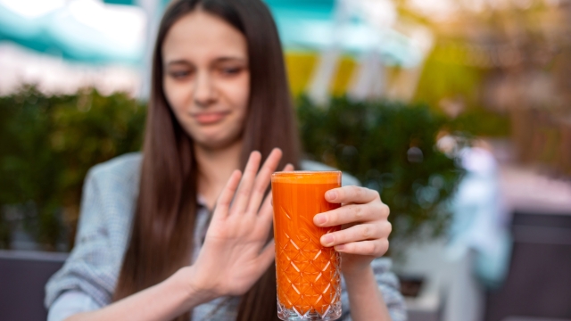 focus on glass with nutrition orange carrot juice. teen girl dislike healthy drink. allergy to ingredients