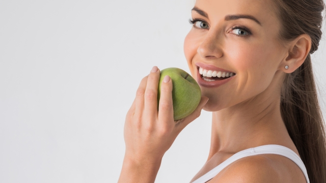 Young woman with healthy teeth smiling and biting green apple