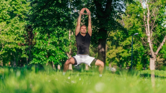 A young man practices yoga with the variations of the goddess pose outdoor in the park
