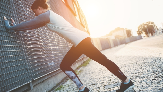 Young woman doing legs warming exercise, safety stretching before running on the street