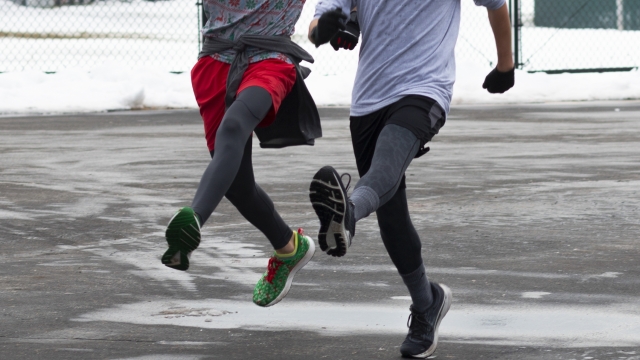 Two high school boy runners bounding in a wet and icy parking lot after a snow storm.