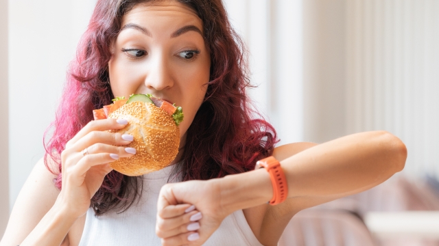 The girl was in a hurry looking at wristwatch and finishing to eat her burger in a fast food cafe