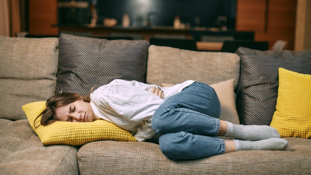 Unhealthy young woman suffering menstrual pain, feeling sick to stomach, holding belly, having abdominal cramps during period lying on couch. High quality photo