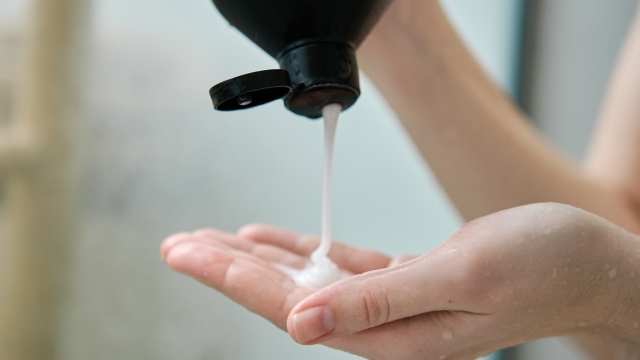 Pouring shampoo from bottle on female hand in bathroom. Hygiene concept
