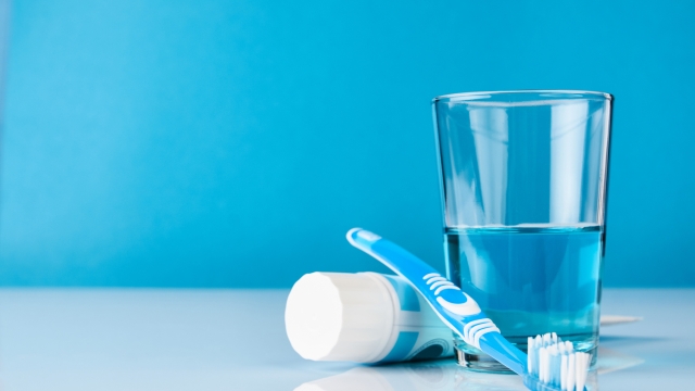 A blue toothbrush with toothpaste and glass of blue mouthwash on blue background with copy space, close-up. Dental oral hygiene concept