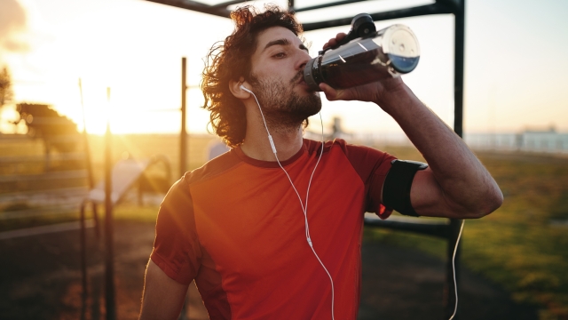 Young man drinking water after exercising in the outdoor gym park