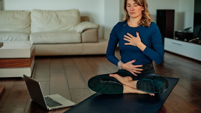 Middle-aged brunette sitting in lotus poses and meditating at home while following video tutorials.