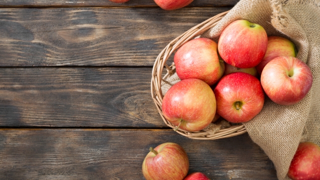 Red apples in a basket on a brown wooden table closeup. Autumn harvest