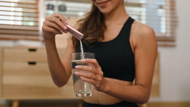 Young woman dissolving collagen powder in glass of water, preparing healthy supplement after exercise.