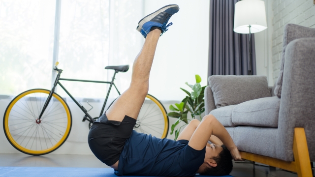Young well-built man exercise at home. He uses a sofa. Abdominal exercises.