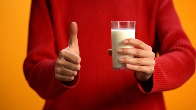 Female holding glass of fresh milk showing thumb up, diary refreshment, calcium