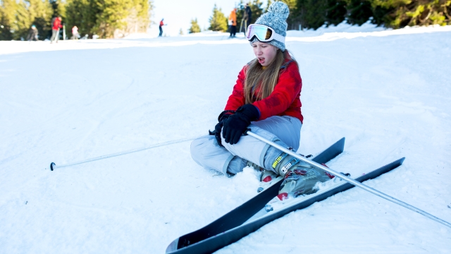 Teenage ski girl holding her knee in pain after accident on ski slope.