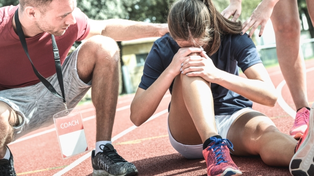 Female athlete getting injured during athletic run training - Male coach taking care on sport pupil after physical accident - Team care concept with young sporty people facing mishaps casualty