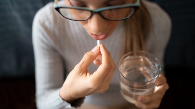 A Young Sick White Woman at Home Swallowing Her Medical Treatment Pills With a Glass of Water. Concept of Medicine, Drugs Adherence, Antibiotics and Pain Killer Addiction.