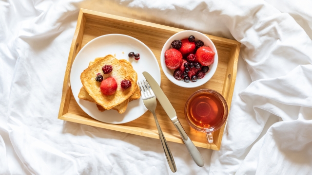 Bright color breakfast in bed. Toast with strawberry, blueberry, black raspberry and a cup of tea in clear glass cup on a wooden tray
