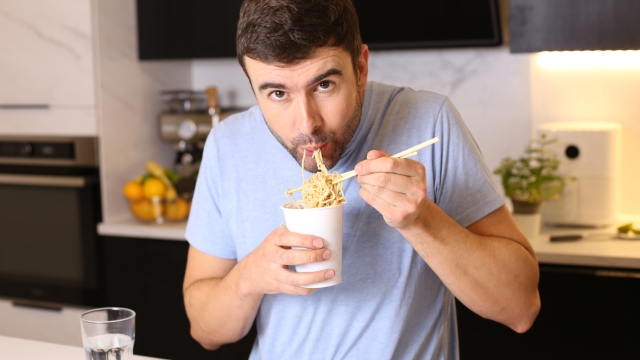 A cute single guy in his forties is eating instant noodles in his modern looking kitchen.