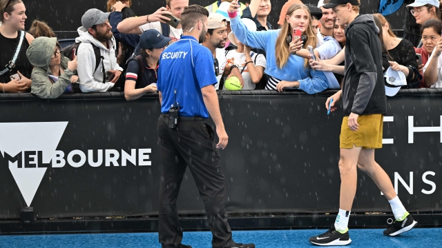 Italy's Jannik Sinner (R) signs autographs to fans as he leaves the court due to the rain during a training session on day 12 of the Australian Open tennis tournament in Melbourne on January 25, 2024. (Photo by Paul Crock / AFP) / -- IMAGE RESTRICTED TO EDITORIAL USE - STRICTLY NO COMMERCIAL USE --