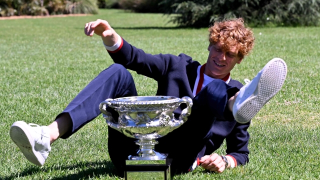 TOPSHOT - Italy's Jannik Sinner makes himself confortable to pose with the Norman Brookes Challenge Cup trophy at the Royal Botanic Gardens following his victory against Russia's Daniil Medvedev in the men's singles final match of the Australian Open tennis tournament in Melbourne on January 29, 2024. (Photo by WILLIAM WEST / AFP) / -- IMAGE RESTRICTED TO EDITORIAL USE - STRICTLY NO COMMERCIAL USE --