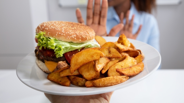 Young Woman Refusing Burger And French Fries On Plate