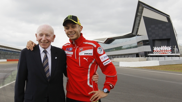 FILE - This is a Tuesday, May 17, 2011 file photo of former British Formula One and Motorcycle world champion John Surtees with former Moto GP world champion Valentino Rossi as they pose for the cameras as the the new pit lane complex at Silverstone race track is opened at Silverstone England.  Surtees, the only man to win world titles on both two and four wheels, has died aged 83, his family said Friday.  Surtees won the Formula One title in 1964 to add to his 500cc motorcycle world titles from 1956, 1958, 1959 and 1960.  (AP Photo/Alastair Grant, file)