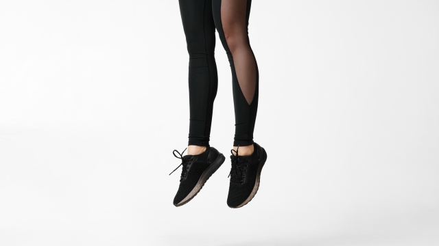 slim female legs in black sport leggings and running shoes jumping on white background