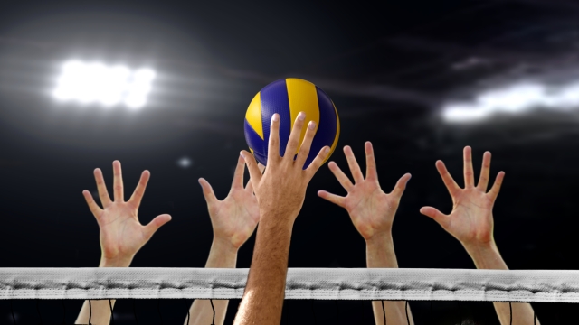 Close up of Volleyball spiking and hand blocking over the net under bright spotlights