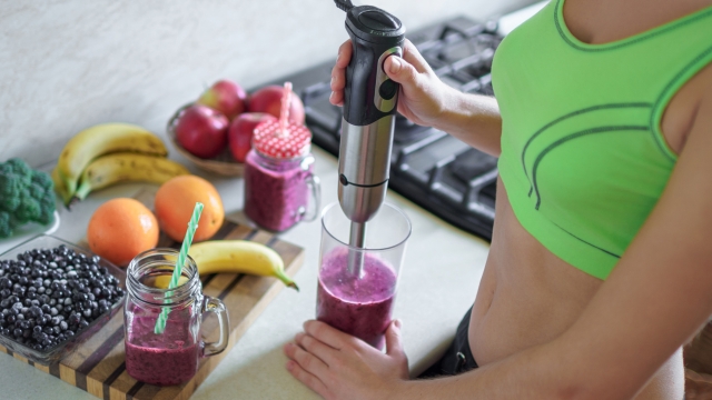 Sports healthy woman cooking fresh blueberry smoothie using hand blender at home. Clean organic eating, food control and berry drinks