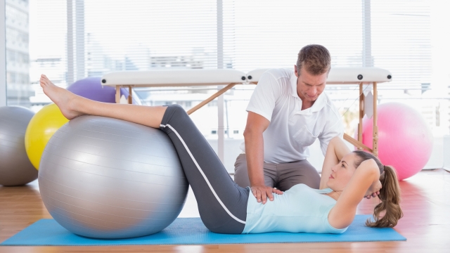 Trainer working with woman on exercise mat in fitness studio
