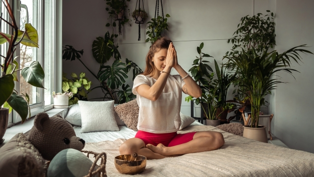 Young sporty woman practicing yoga at home,sitting in Lotus position,namaste hands.Relaxation and meditation.Wellness,wellbeing,mental health concept.