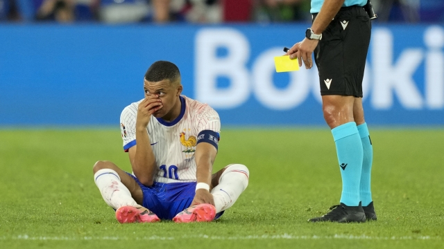 Kylian Mbappe of France sits on the pitch, hand over his bloody nose, as the referee holds the yellow card, during a Group D match between Austria and France at the Euro 2024 soccer tournament in Duesseldorf, Germany, Monday, June 17, 2024. (AP Photo/Andreea Alexandru)