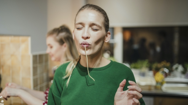 Young woman is posing for the camera with spaghetti hanging out her mouth.