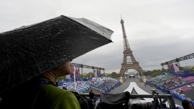A photographer waits in the rain in Paris, France, before the opening ceremony of the 2024 Summer Olympics, Friday, July 26, 2024. (AP Photo/David J. Phillip)