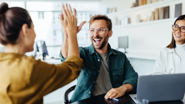 Successful business people giving each other a high five in a meeting. Two young business professionals celebrating teamwork in an office.