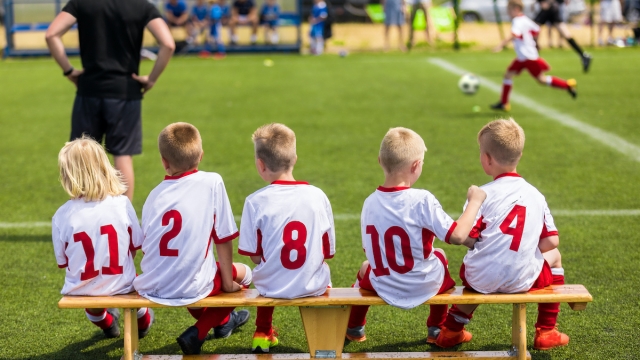 Children Soccer Team Watching Football Match. Children Sport Team in White Shirts. Youth Soccer School Tournament for Children. Young Boys in Soccer Jersey. Football Wooden Bench