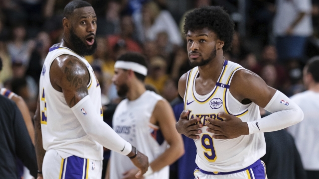 Los Angeles Lakers guard Bronny James (9), right, steps onto the court with Los Angeles Lakers forward LeBron James (23) during the first half of a preseason NBA basketball game Sunday, Oct. 6, 2024, in Palm Desert, Calif. (AP Photo/William Liang)